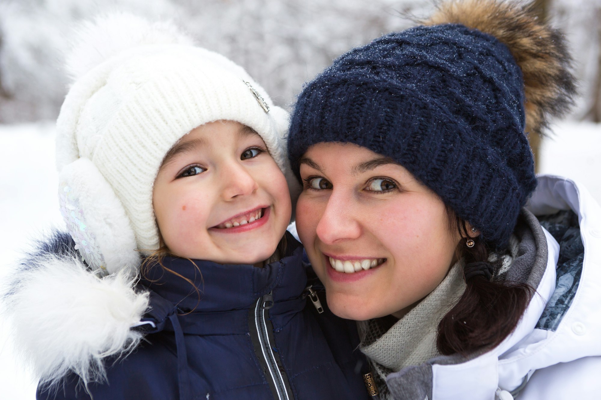 Mom and daughter in warm clothes in the snowy forest hugging and looking